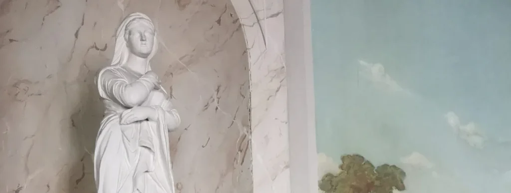 Weiße Frauenstatue in einer marmorierten Wandnische neben einem Wandgemälde mit Wolkenhimmel.