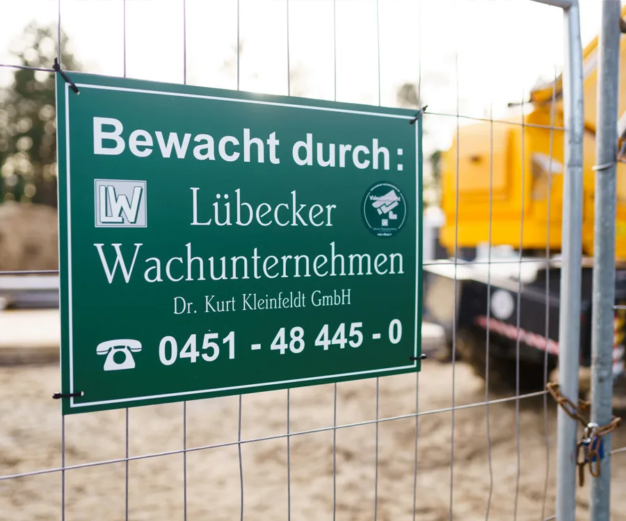 Baubewachung des Lübecker Wachunternehmens: grünes Hinweisschild am Bauzaun mit Kontaktangaben und Videoüberwachung.