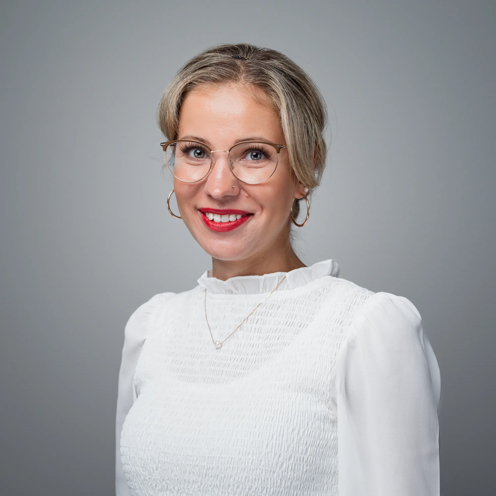 Porträt von Inna Einik, einer lächelnden jungen Frau mit blonden Haaren, Brille und rotem Lippenstift, die in die Kamera blickt.