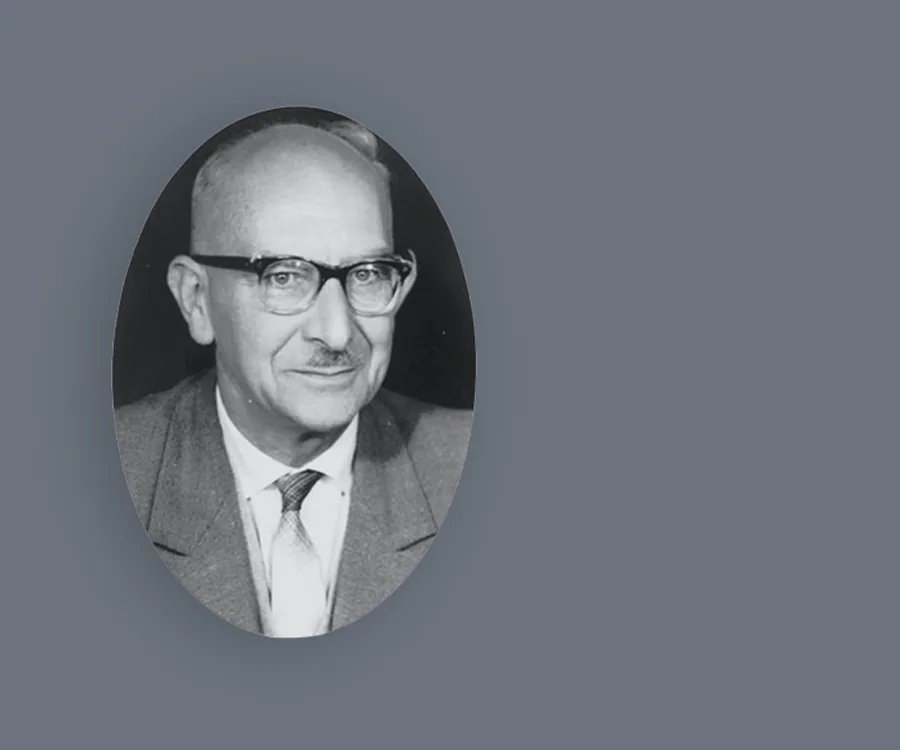 Schwarz-Weiß-Porträt eines älteren Mannes mit Brille und Schnurrbart, der einen Anzug und eine Krawatte trägt und leicht nach rechts blickt.