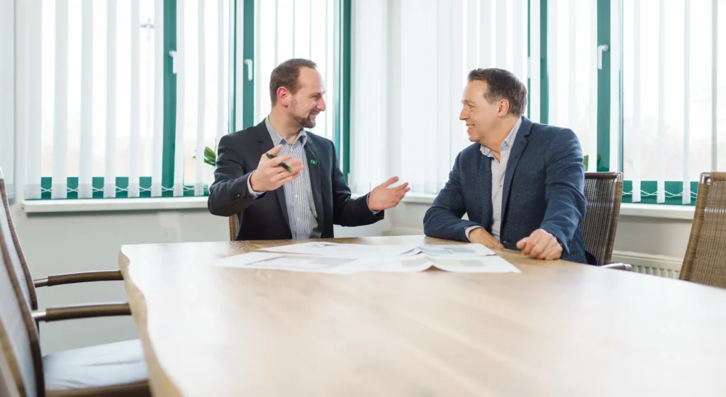 Zwei Männer in Business-Kleidung sitzen an einem Holztisch und führen ein professionelles Beratungsgespräch zur Gefahrenanalyse.