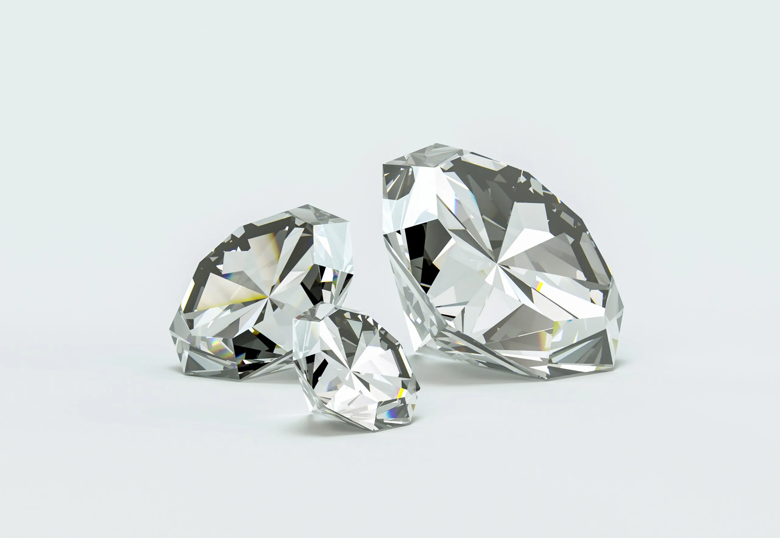 Drei funkelnde Diamanten im Brillantschliff liegen nebeneinander auf einem hellen, neutralen Untergrund.