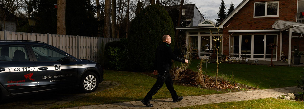 Sicherheitsmitarbeiter auf Rundgang neben einem Einsatzfahrzeug vor einem Wohnhaus.