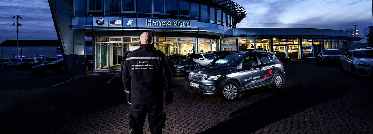 Sicherheitsmitarbeiter und Einsatzfahrzeug vor einem Autohaus bei Dämmerung.