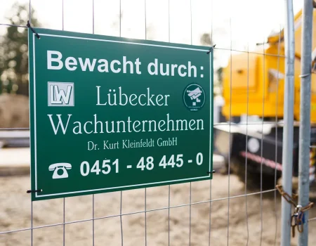 Baubewachung des Lübecker Wachunternehmens: grünes Hinweisschild am Bauzaun mit Kontaktangaben und Videoüberwachung.