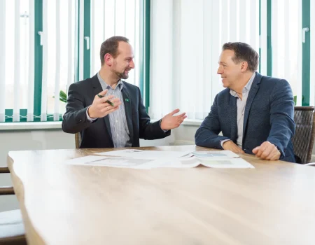 Zwei Männer in Business-Kleidung sitzen an einem Holztisch und führen ein professionelles Beratungsgespräch zur Gefahrenanalyse.