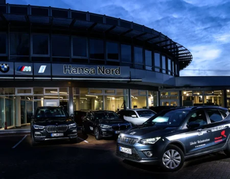 Ein beleuchtetes Autohaus von Hansa Nord bei Nacht, mit mehreren geparkten Autos und einem Fahrzeug des Lübecker Wachunternehmens im Vordergrund.